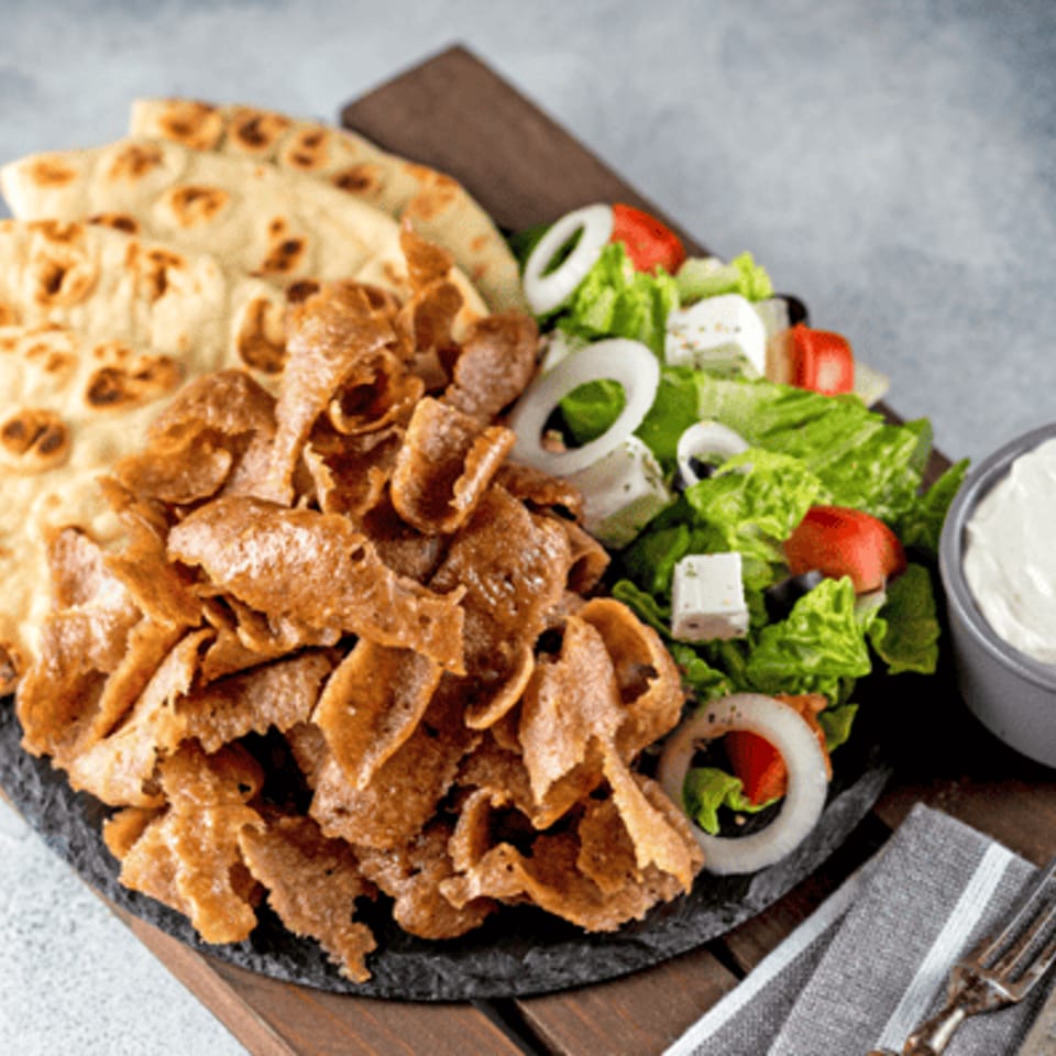 Döner kebab plate with shaved meat, flatbread, fresh Greek salad, and creamy white sauce.
